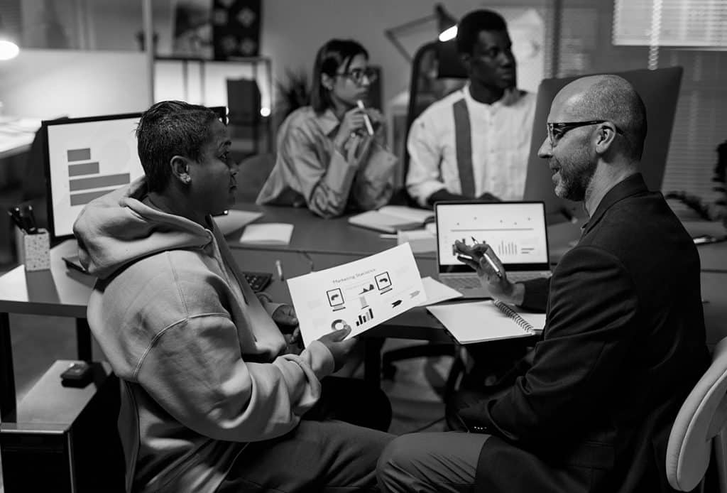 Diverse group of business professionals discussing digital and printed charts at a table.